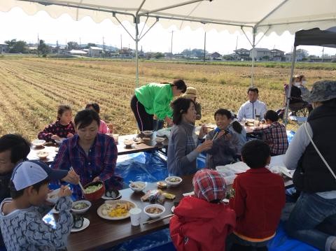 稲刈りの後に参加者全員で和気あいあいとお昼ご飯を食べている写真